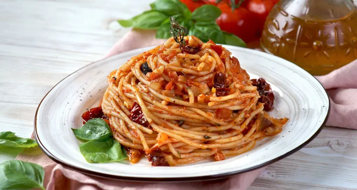 Un piatto di spaghetti conditi con un sugo rosso ricco di pomodori secchi, aglio e basilico fresco.