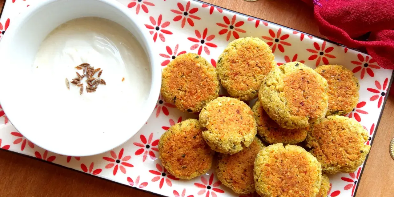 Falafel al forno dorati su un piatto decorato, accompagnati da una ciotola di salsa bianca con semi di cumino.