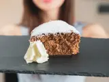 Una fetta di pan di spagna al cacao, soffice e spolverata di zucchero a velo, servita con panna montata su una lavagna scura.