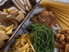 Varietà di pasta cruda, tra cui conchiglioni, paccheri, fettuccine verdi e gialle, lasagne e fusilli, pronte per essere condite con i migliori sughi per pasta.