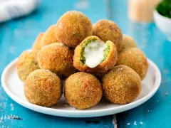 Pile di polpette di broccoli dorate e croccanti, una con il cuore filante di formaggio.