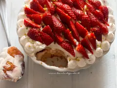 Delizioso tiramisù alle fragole, con panna montata, fragole fresche e pistacchi. Una fetta è già servita su un cucchiaio.