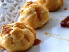 Bignè alla crema soffici e dorati, bagnati da un filo di caramello lucido su un piatto bianco.