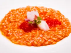 Un cremoso risotto al pomodoro, guarnito con calamari teneri, pomodorini e germogli freschi. Un piatto che celebra i sapori dell'Italia.