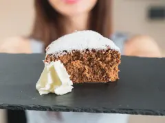 Una fetta di pan di spagna al cacao, soffice e spolverata di zucchero a velo, servita con panna montata su una lavagna scura.