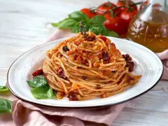 Un piatto di spaghetti conditi con un sugo rosso ricco di pomodori secchi, aglio e basilico fresco.