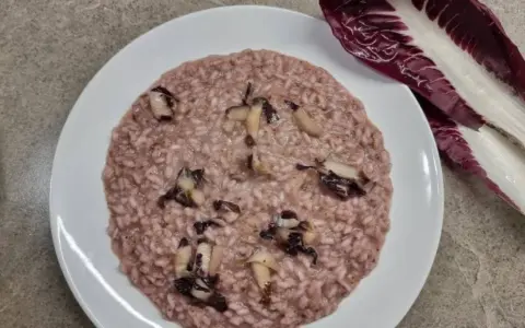 Un cremoso risotto al radicchio, con pezzetti di verdura che spuntano dal riso. Accanto, una foglia di radicchio fresco.