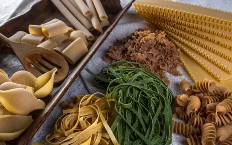 Varietà di pasta cruda, tra cui conchiglioni, paccheri, fettuccine verdi e gialle, lasagne e fusilli, pronte per essere condite con i migliori sughi per pasta.