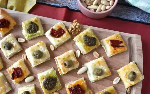 Sfiziose ricette con pasta sfoglia: quadratini dorati con olive, pesto e pomodori secchi, perfetti per un aperitivo.