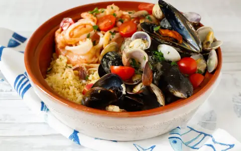 Un invitante cous cous di pesce, ricco di cozze, vongole, gamberi e pomodorini, guarnito con prezzemolo fresco.