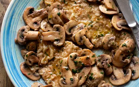 Scaloppine ai funghi, un piatto succulento con fettine di carne dorate e funghi champignon trifolati, guarnito con prezzemolo fresco.