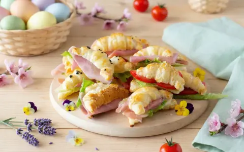 Delizioso antipasto di Pasqua con croissant farciti, uova colorate in un cesto e fiori primaverili.