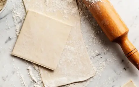 Farinata e mattarello su piano di marmo, pronti per creare pasta sfoglia fatta in casa.