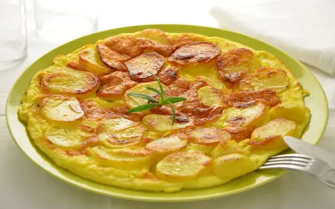 Frittata di patate dorata e gustosa, guarnita con rosmarino fresco, servita su un piatto verde.