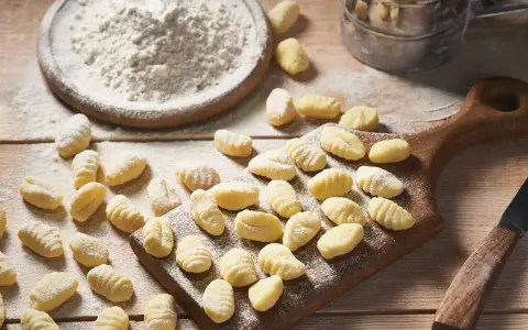 Gnocchi senza glutine appena fatti, spolverati di farina, su un tagliere di legno.