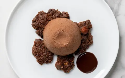 Semifreddo al cioccolato su croccanti biscotti al cacao, con una nocciola intera e una goccia di salsa al cioccolato.