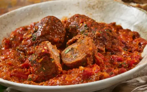 Involtini alla romana succulenti in un ricco sugo di pomodoro, con un interno visibile che rivela erbe aromatiche.