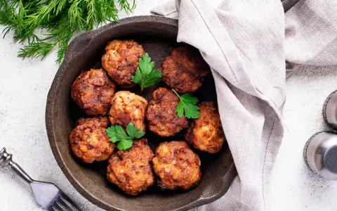 Polpette senza uova dorate in padella, guarnite con prezzemolo fresco. Un piatto gustoso e leggero, pronto per essere gustato.