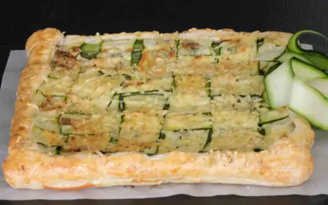 Torta salata con pasta sfoglia e zucchine a griglia, ricoperta di formaggio fuso e guarnita con fettine di zucchina fresca.
