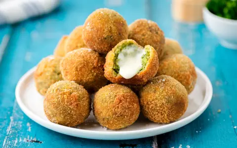 Pile di polpette di broccoli dorate e croccanti, una con il cuore filante di formaggio.