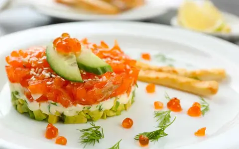 Tartare di salmone e avocado, un'idea per antipasti velocissimi senza cottura, guarnita con uova di pesce e cetriolo.