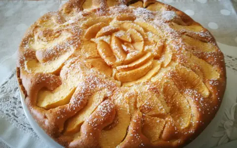 Deliziosa torta di mele senza glutine, decorata con mele a forma di rosa e spolverata di zucchero a velo.