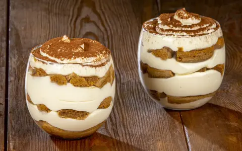 Due bicchieri di delizioso tiramisù senza uova, con strati di savoiardi e crema, spolverati di cacao.