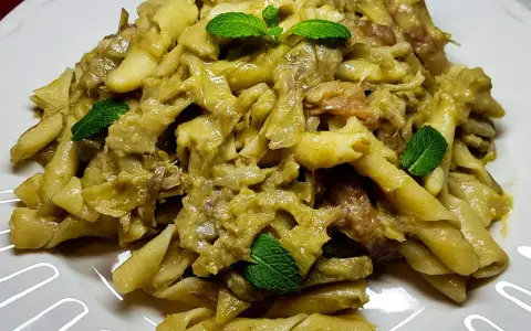 Pasta con carciofi cremosa, guarnita con foglie di menta fresca. Un piatto saporito e invitante.