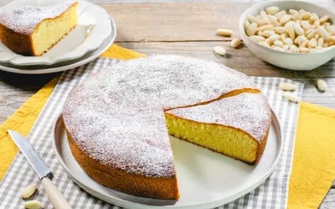Torta soffice con farina di mandorle, spolverata di zucchero a velo. Un pezzo è già stato tagliato, pronto per essere gustato.