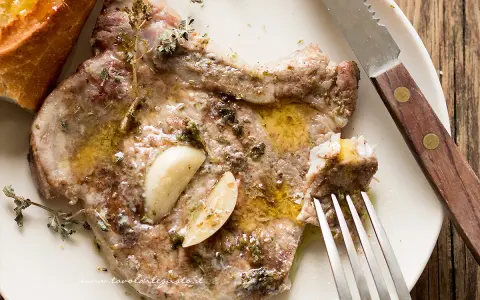 Succulente braciole di maiale cotte con aglio e erbe aromatiche, servite con pane croccante.