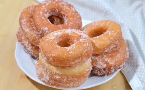 Ciambelle fritte dorate, cosparse di zucchero, pronte per essere gustate. Una deliziosa ricetta ciambelle fritte per ogni occasione.