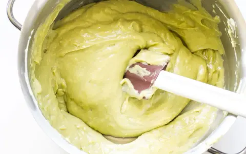 Una spatola mescola una densa crema al pistacchio in una ciotola d'acciaio.
