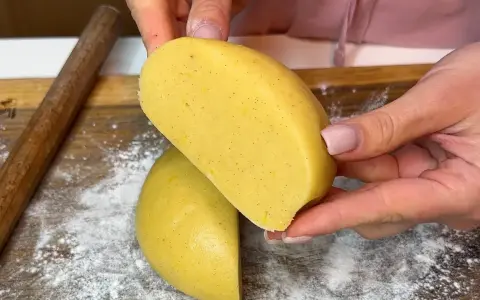 Mani che tengono un impasto giallo, profumato alla vaniglia, pronto per diventare una deliziosa pasta frolla senza burro.