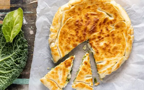 Torta salata con pasta sfoglia dorata, ripiena di verdure. Accanto, foglie di cavolo nero fresco.