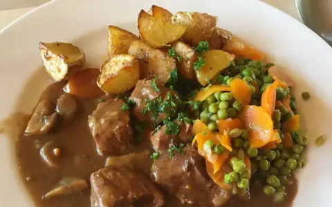 Un saporito spezzatino con piselli, carote e patate arrosto, guarnito con prezzemolo fresco.