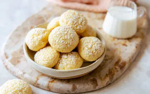 Biscotti da inzuppo spolverati di zucchero a velo in una ciotola, pronti per essere gustati con un bicchierino di latte.