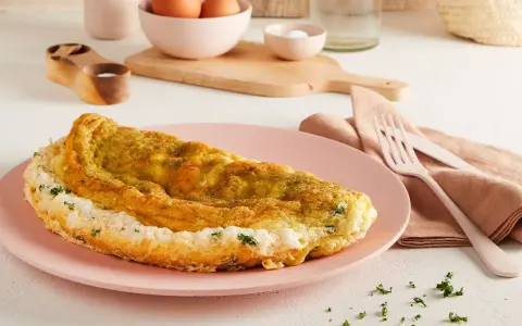 Frittata soffice e dorata, preparata in friggitrice ad aria, servita su un piatto rosa con erbe fresche.