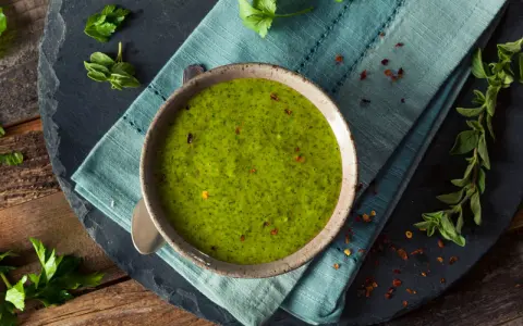 Una ciotola di vibrante salsa verde senza uovo, guarnita con peperoncino rosso tritato e erbe fresche. Perfetta per accompagnare i tuoi piatti preferiti.