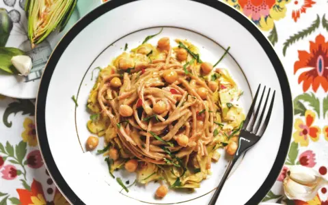 Un piatto invitante di pasta con carciofi alla siciliana, arricchito da ceci e erbe fresche, su un tovagliolo fiorito.