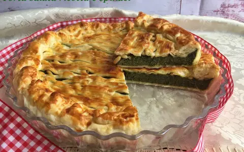 Torta salata ricotta e spinaci dorata e invitante, con una fetta tagliata che mostra il ripieno verde e cremoso.