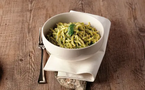 Un piatto invitante di trofie al pesto, guarnito con una foglia di basilico, su un tavolo di legno rustico.