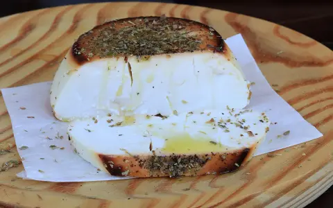 Ricotta al forno dorata e profumata con erbe aromatiche, servita su un tagliere di legno.