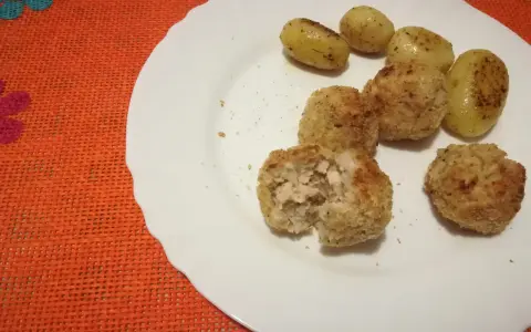 Piatto con polpette di pollo dorate e patate novelle condite. Una polpetta è stata aperta, mostrando l'interno succulento.