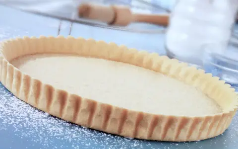 Base per crostata pronta, una deliziosa pasta frolla senza uova, cosparsa di zucchero a velo su un piano blu.