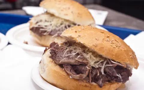 Panino con la milza, un classico street food siciliano, servito su un panino morbido con semi di sesamo e abbondante formaggio grattugiato.