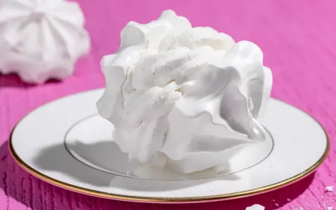 Dolci meringhe bianche, perfette per le tue ricette con albumi, su un piatto con bordo dorato, su sfondo fucsia.