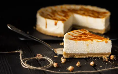 Una fetta di cheesecake senza panna, con glassa caramellata, su un piatto da portata. Sullo sfondo, la torta intera.