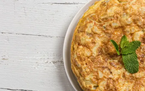 Frittata di cipolle dorata e soffice, guarnita con foglie di menta fresca, su un tavolo di legno bianco.