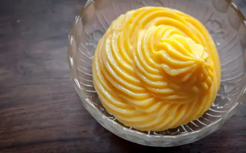 Crema pasticcera ricetta: una deliziosa crema gialla, liscia e lucida, servita in una ciotola di vetro trasparente con decori.