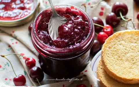 Un barattolo pieno di deliziosa marmellata di ciliegie, con ciliegie fresche e fette biscottate accanto.